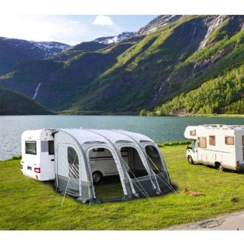 Förtält med bågar och fönster vid husvagn nära sjö och berg.